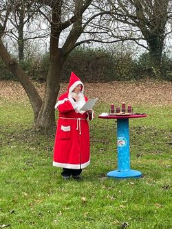 Adventsschwimmen 2024 Das Bild zeigt Bademeisterin Elke Sparkuhl im Weihnachtsmann-Kostüm an einem bunten Stehtisch stehend.