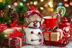 Das Bild zeigt ein weihnachtliches Motiv mit kleinen hübsch eingepackten Geschenken und einem kleinen Schneemann vor einem Weihnachtsbaum