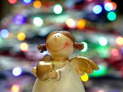 Auf dem bild ist ein Keramik Engel der ein Herz in den Händen hält und im Hintergrund ist eihnachtsbeleuschtung zu sehen.