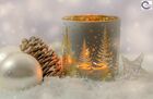 Auf dem Bild sind weißgoldene Christbaumkugeln, ein Tannenzapfen und ein weihnachtliches Teelichtglas zu sehen.